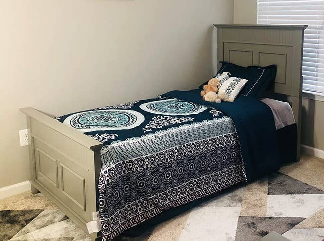 Reviewer image of product in navy blue and teal with navy blue pillow and navy and white medallion throw pillow on a wooden bed frame