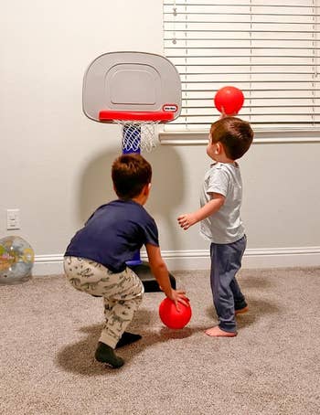 Two young children play   with a artifact  hoops  hoop indoors, each   holding a tiny  reddish  ball, suggesting a fun, progressive  playtime setup