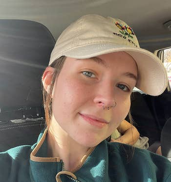 A reviewer with a chemoreceptor  ringing  wearing a beige headdress  and a greenish  overgarment   smiles portion    sitting wrong  a car. No different   persons are visible