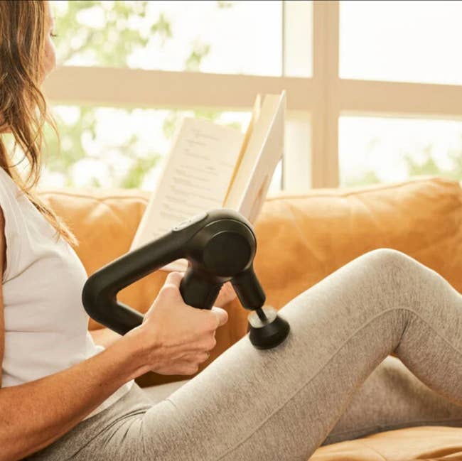 model holding the black massager, using it on their thigh while reading a book