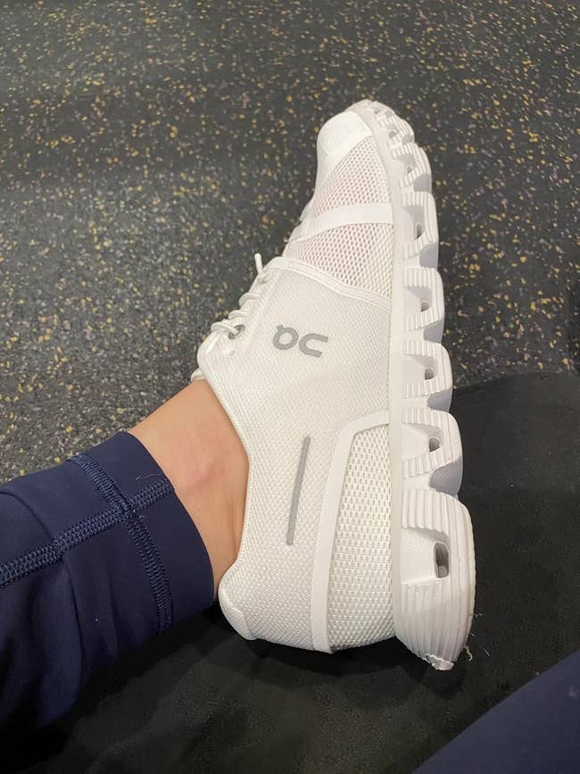 Person wearing a white athletic On Cloud 5 sneaker with a unique hole sole design