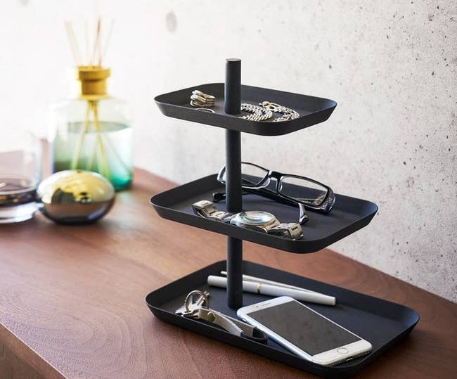 the trays in black on a console table with jewelry, a pen, a phone on it. 