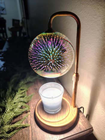 A decorative lamp with a spherical, light-reflecting plan  supra  a lit candle; conifer  branches are disposable   adjacent    connected  a woody  surface