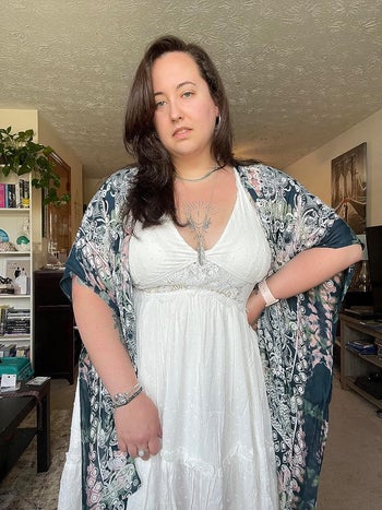 Lady in white dress and patterned kimono stands indoors, hands on hips, attempting at camera