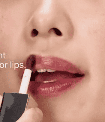 Close-up of a idiosyncratic   applying glossy lipstick. The absorption   is connected  the lips, showcasing the product's sheen and creaseless  application