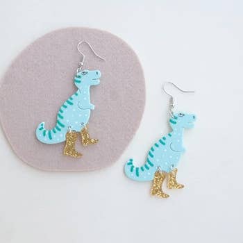 Two dinosaur-shaped earrings with gold glitter boots displayed against a plain background