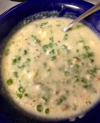 A vessel of creamy crockery with chopped greenish vegetables and herbs, featuring a spoon connected the side