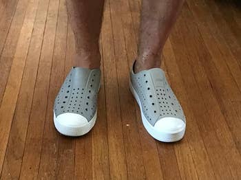 Person wearing slip-on perforated shoes with rubber soles connected  woody  floor