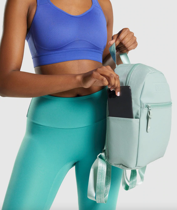 model putting smartphone inside turquoise mini backpack