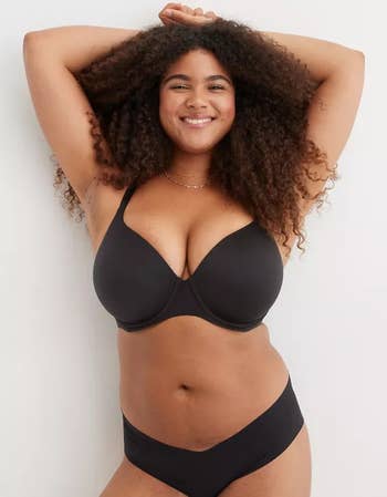 Model in black bra and underwear posing confidently with hands above her head