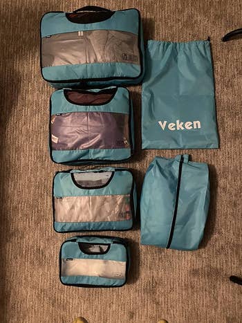 Six Veken packing cubes of varying sizes laid out on a carpeted floor for organization