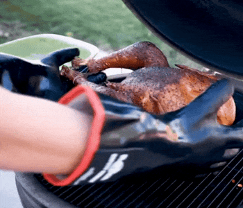 gif of someone wearing the gloves and taking a whole chicken off of a lit grill