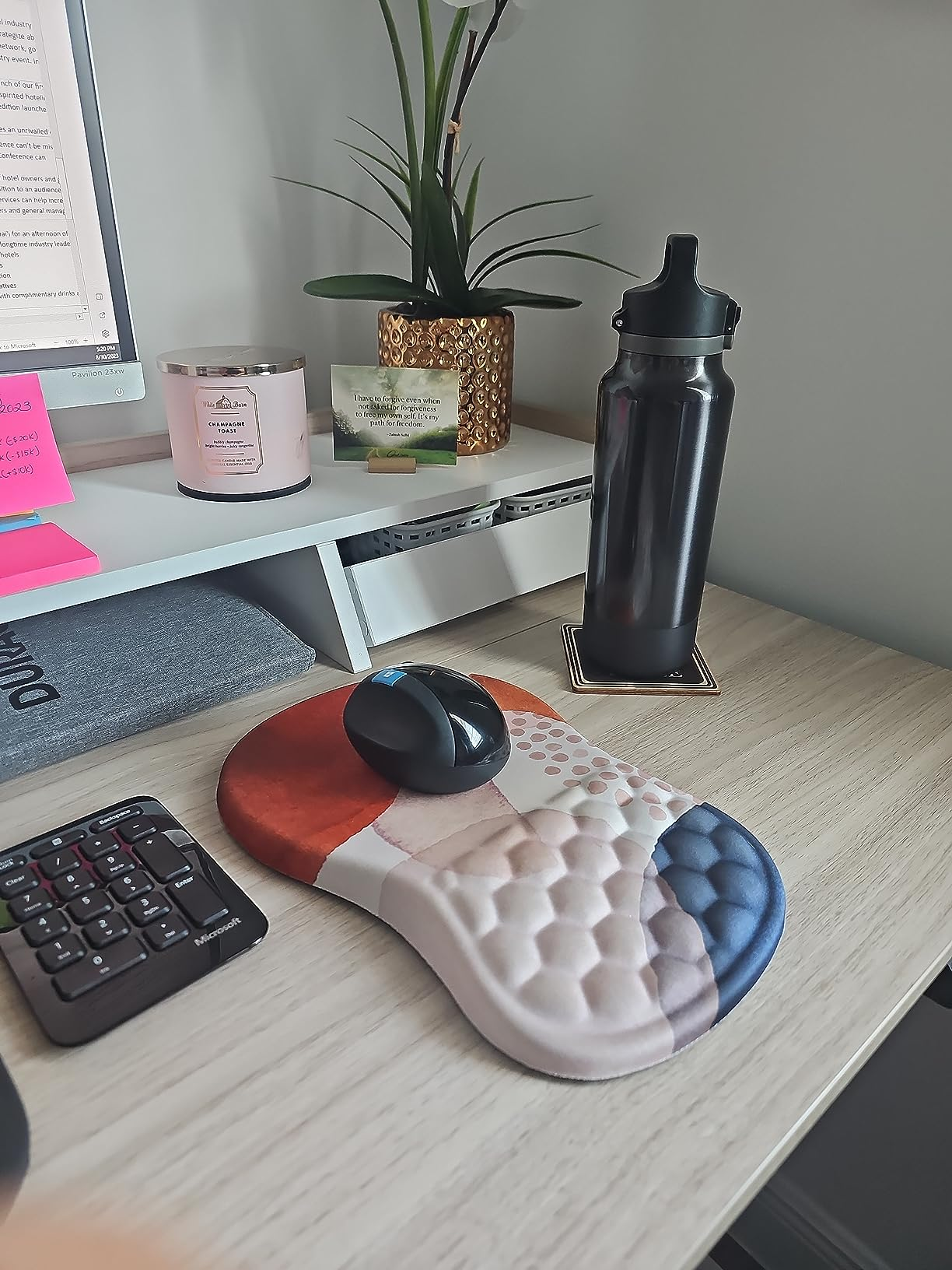 A tidy desk with a computer, ergonomic mouse, and a patterned mousepad; a water bottle and plant decor are present