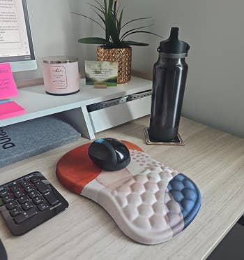 A tidy desk with a computer, ergonomic mouse, and a patterned mousepad; a water bottle and plant decor are present