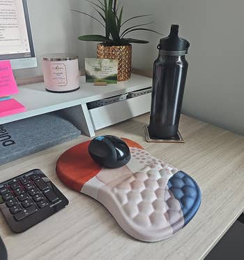 A tidy desk with a computer, ergonomic mouse, and a patterned mousepad; a water bottle and plant decor are present