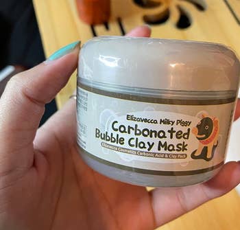 reviewer holding a tub of the clay mask