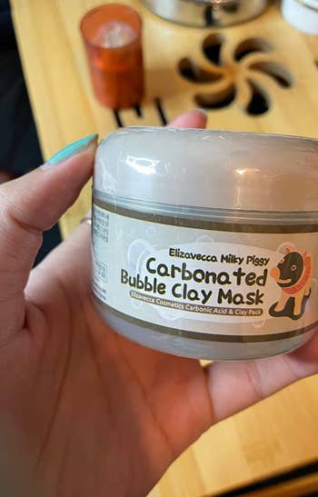 reviewer holding a tub of the clay mask