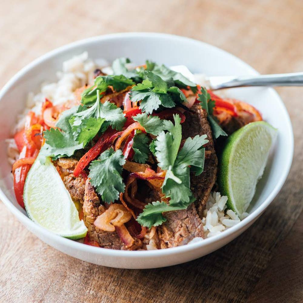 A bowl of rice with meat, veggies, lime and garnish