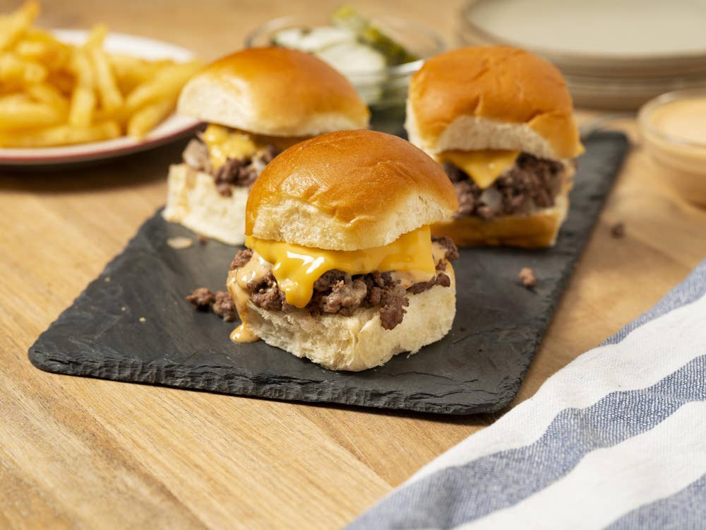 Hamubrger sliders sit on a table in front of a plate of french fries