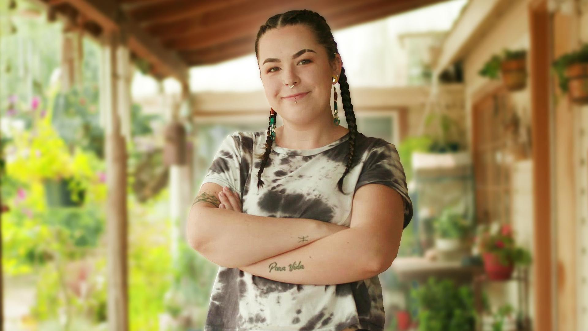 Aiyanna, smiling at the camera, stands on her porch with her arms crossed