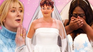 woman on left of frame looks toward woman in center frame in wedding dress.  A third woman on right of frame appear emotional while wearing her own wedding dress.