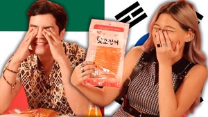 Man of left of frame hides face behind hands while woman on right of frame laughs as she hold up the package of a spicy snack.