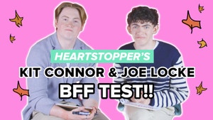 Kit Connor and Joe Locke are seated next to each other on a pink background text reads heartstoppers kit connor and joe jocke BFF test