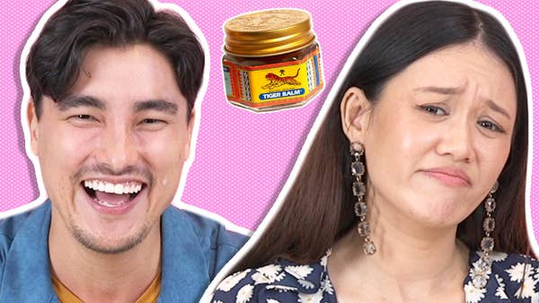 A close up of Remy Hii smiling and Natalie Tran frowning slightly; in the background there is a jar of Tiger Balm
