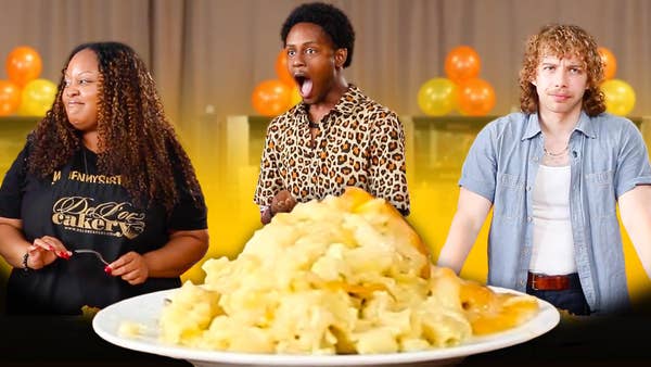 Three participants, two "family" and one "plus one" stand making various facial reactions to the enlarged mac 'n' cheese in the bottom center of the frame. 