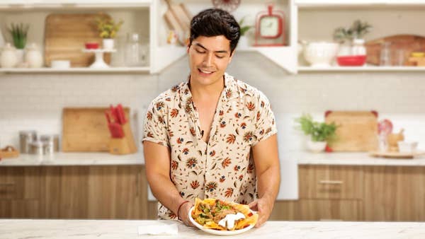 Bachelor Chris Ortiz holds a plate of nachos in a kitchen, smiling.