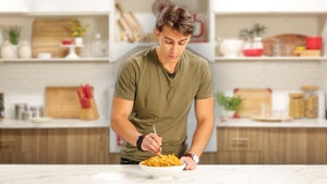 Italian bachelor, Elia, forks a bowl of pasta in a kitchen.