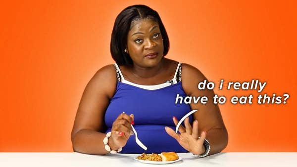 Eustacia, a Caribbean mom representing Trinidad and Tobago, looks disapprovingly at a plate of saltfish made by another contestant. A text bubble reading "do i really have to eat this?" hovers over the dish.