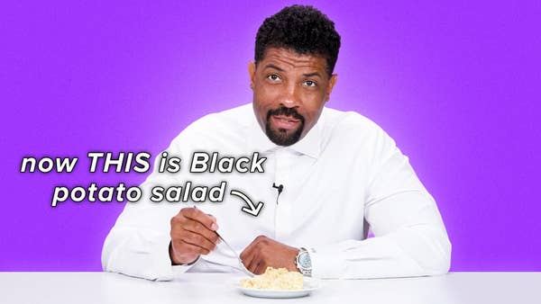 Deon Cole pokes at potato salad with his fork in a white shirt. Text reads, "Now THIS is black potato salad."