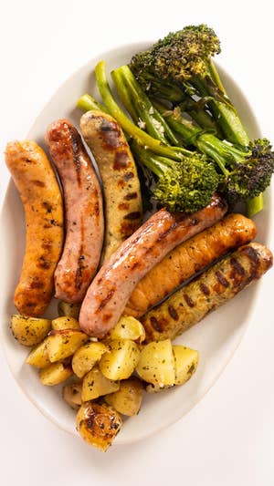 White platter topped with various grilled sausages, grilled potato pieces, and grilled broccolini.