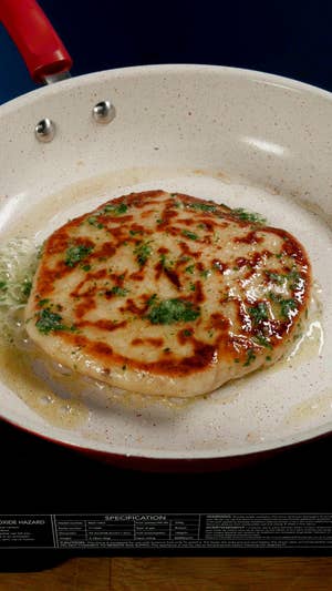 A round white plate topped with a round potato cake, drizzled with melted butter and sprinkled with green herbs.