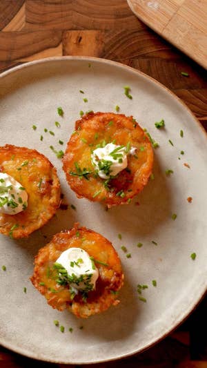 A white plate topped with three tater top muffin cups, each topped with a dollop of sour cream and garnish of green herbs.