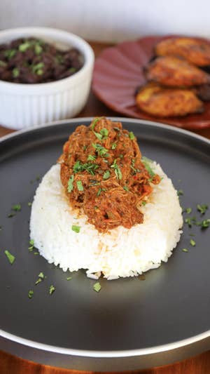 A round plate is topped with a round scoop of white rice, topped with red, saucy shredded beef and a sprinkle of green herbs.