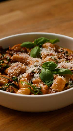 Closeup of a bowl of gnocchi in a textured red sauce with green herbs and grated Parmesan cheese.