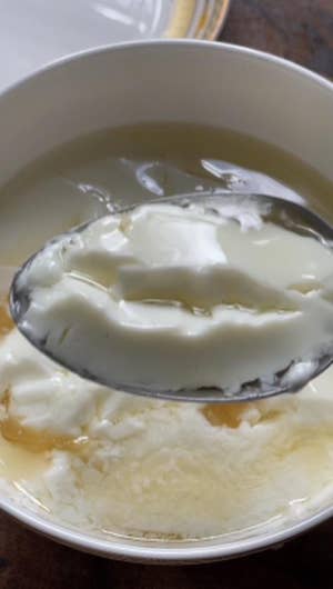 Closeup of a spoon scooping up white milk curd with simple syrup from a small white bowl