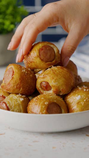 White bowl of miniature hot dogs wrapped in pretzel dough, topped with flaky salt