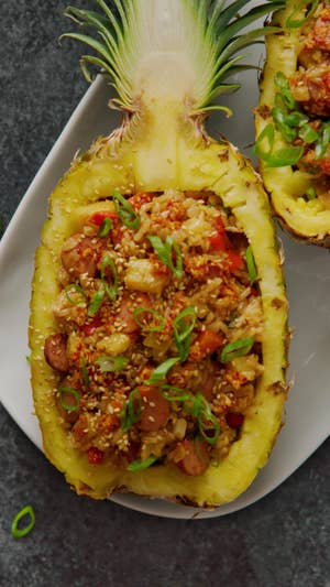 halved and hollowed out pineapple filled with pineapple fried rice with sliced sausage, garnished with scallions