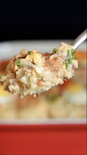 Closeup of a spoon scooping creamy potato salad with small bits of green chives, potatoes, and a dusting of paprika
