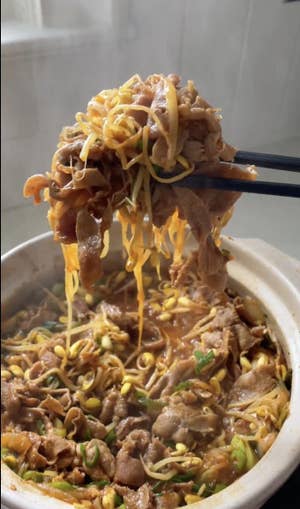 A pot of brothy Kongbul with chopsticks holding up slices of beef and bean sprouts